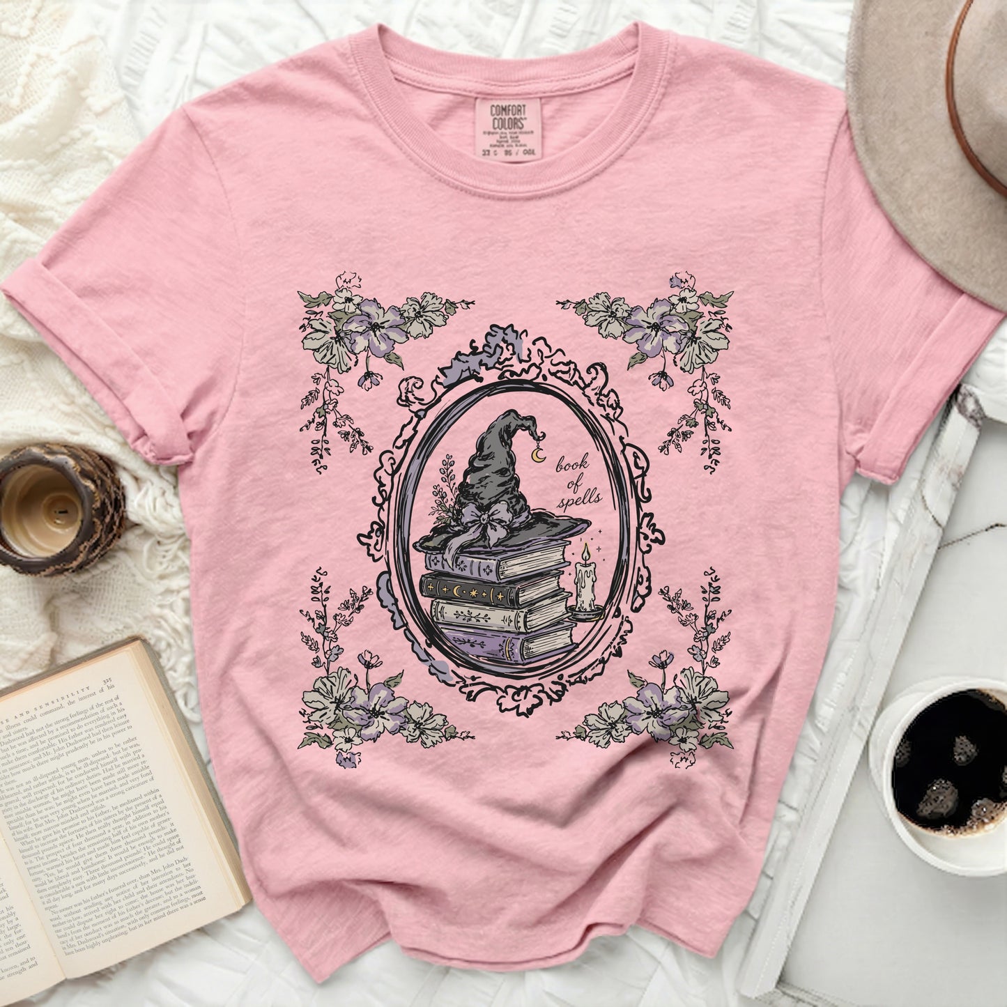 Pink t-shirt with witch hat, books, candle, and floral design.