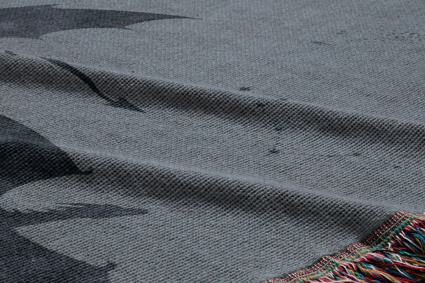 a close-up view of a gray fabric with a black bat silhouette printed on it. The fabric appears to be made of a woven material, and there is a fringe at the bottom of the fabric.