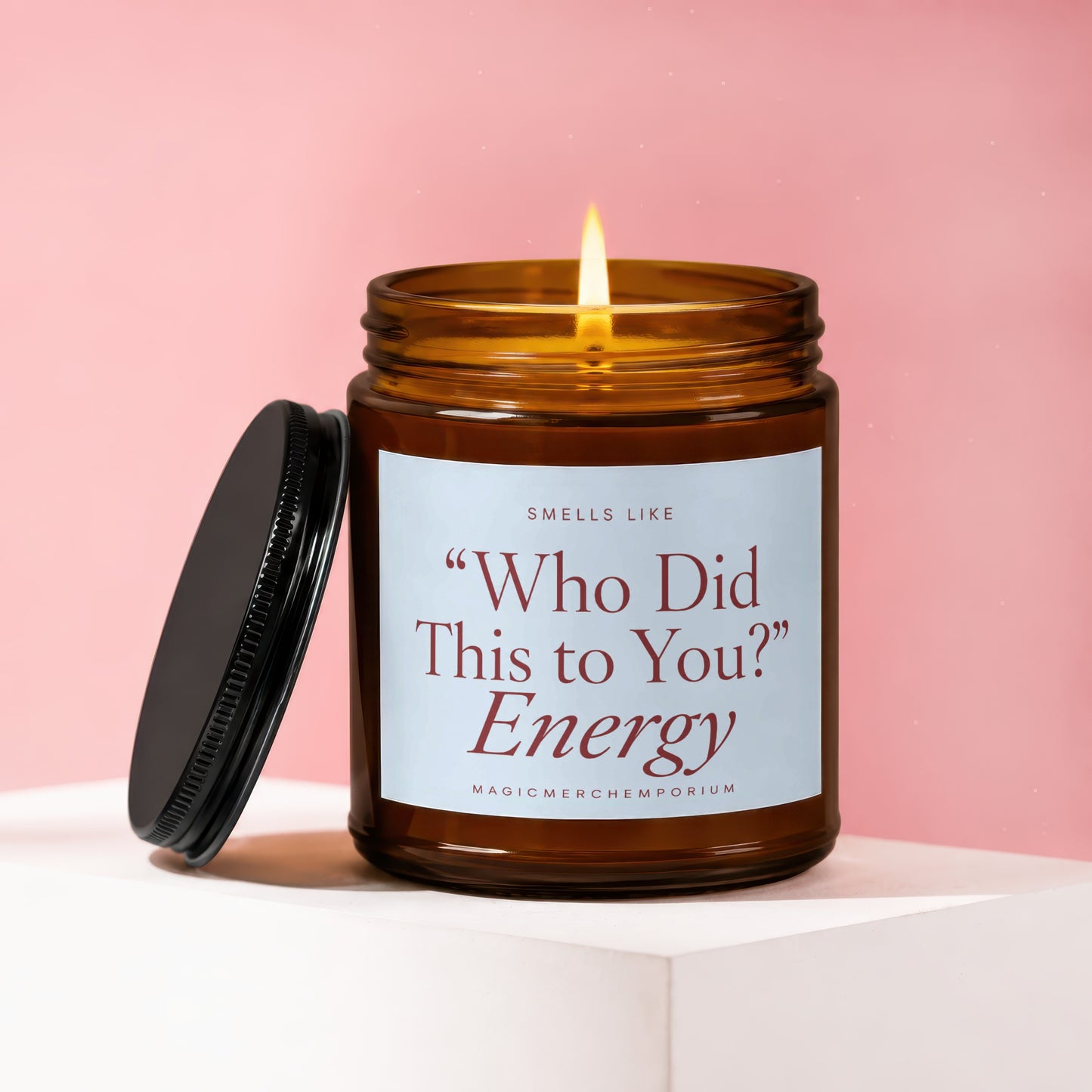 Amber candle with lit wick, lid ajar, reads "Who Did This to You?" Energy