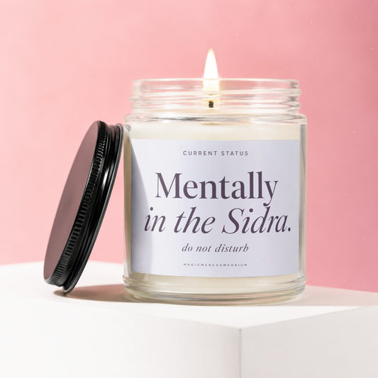 Glass candle with lit wick, lid off, labeled "Mentally in the Sidra. do not disturb."
