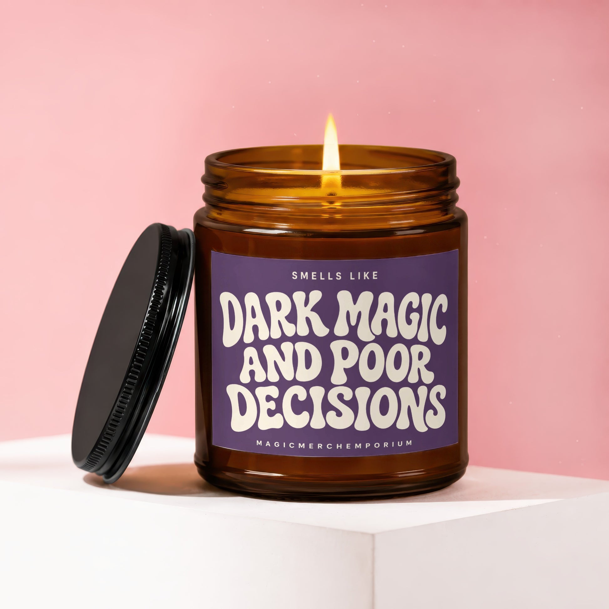 Amber glass candle with lit wick, reads "Smells Like Dark Magic and Poor Decisions".
