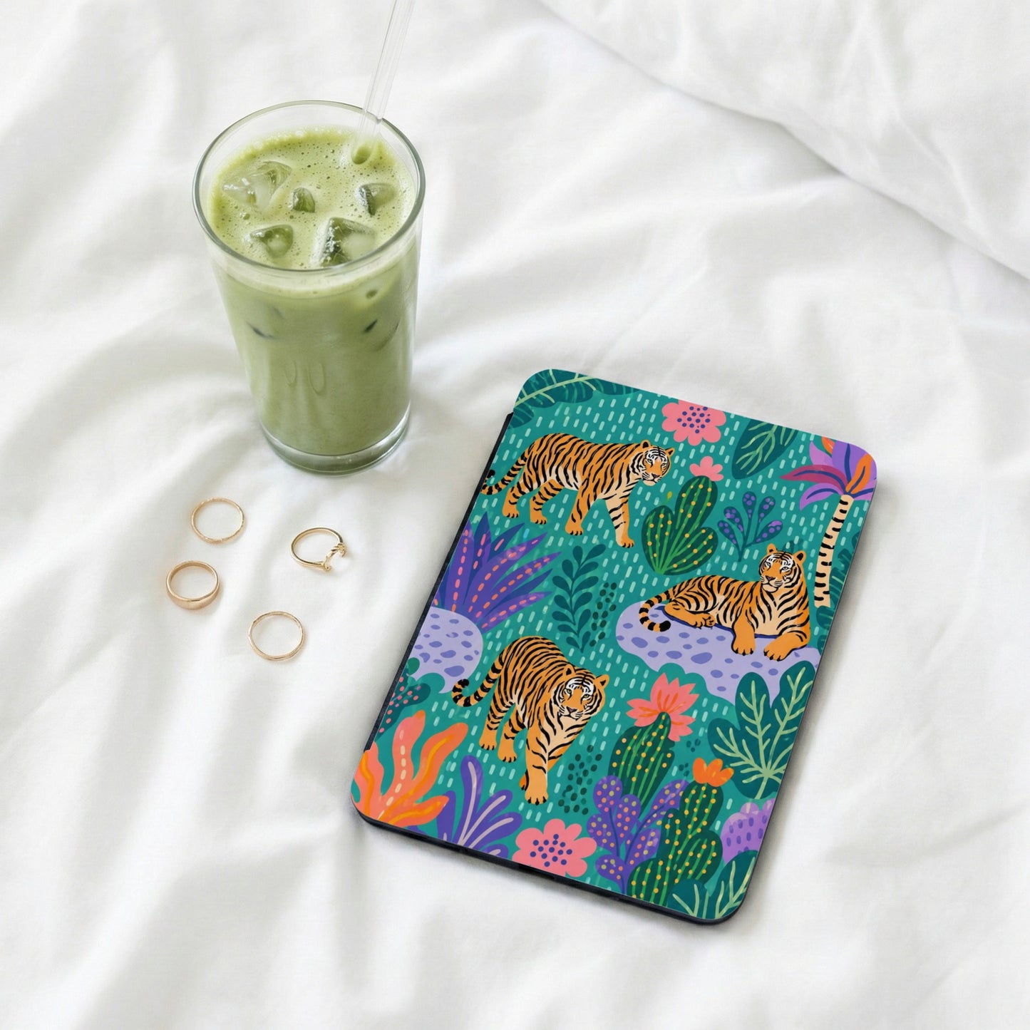 Tablet case with tigers and tropical plants on teal background, beside iced green drink and rings.