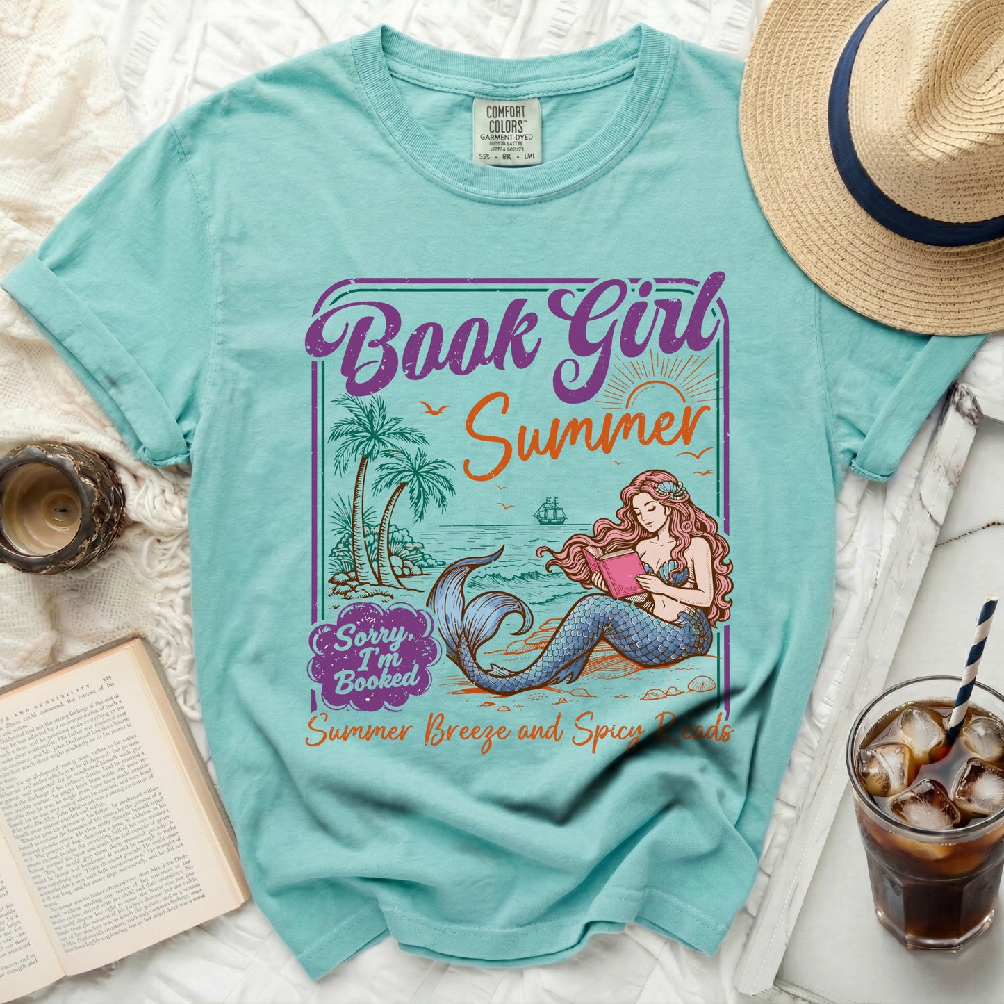 T-shirt with mermaid reading a book, palm trees, and ocean scene.