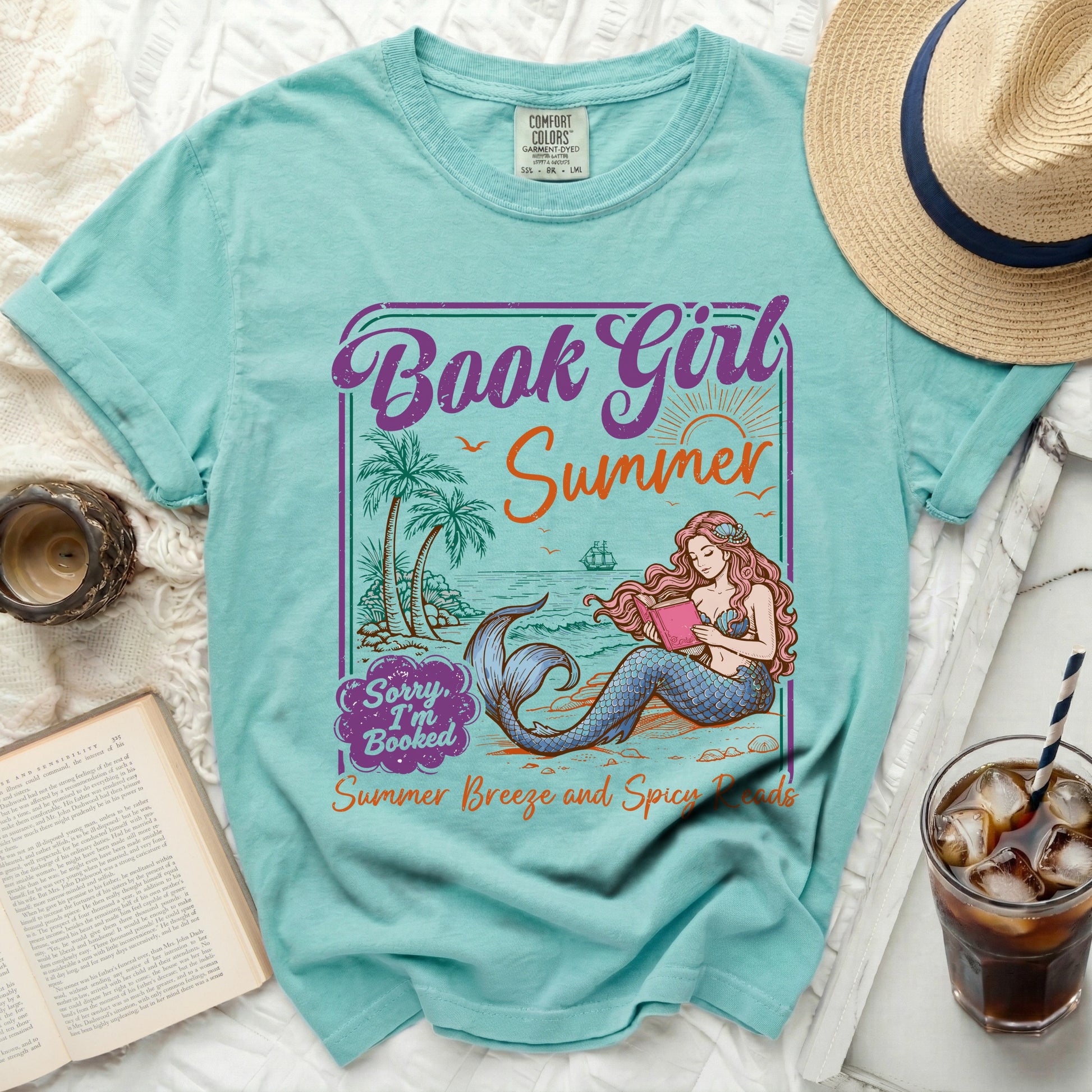T-shirt with mermaid reading a book, palm trees, and ocean scene.