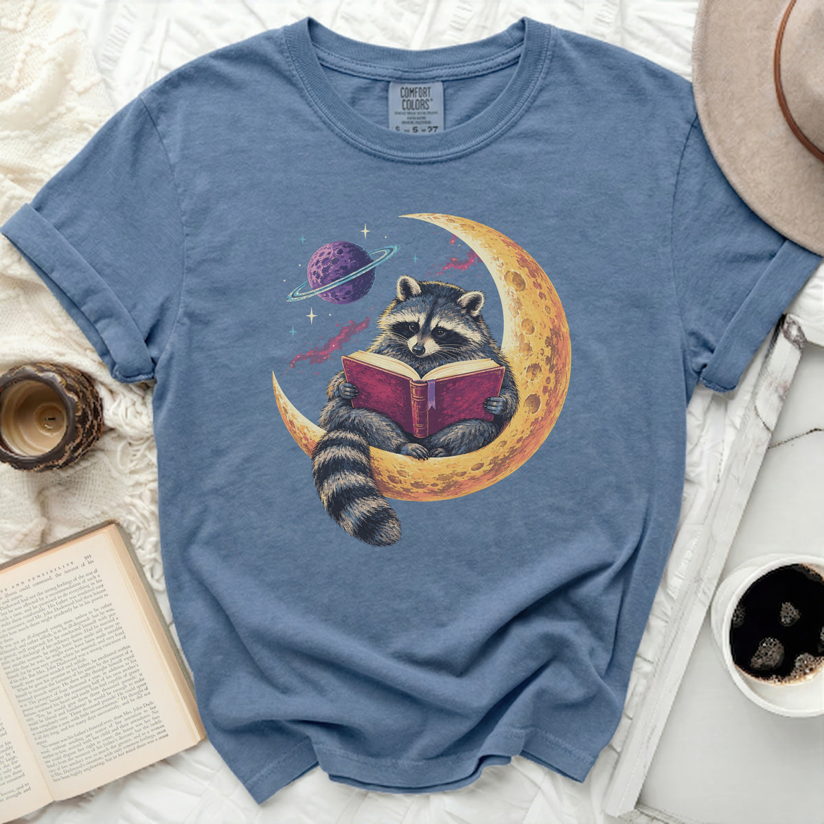 Raccoon sitting on a crescent moon reading a book, with a planet in the background.
