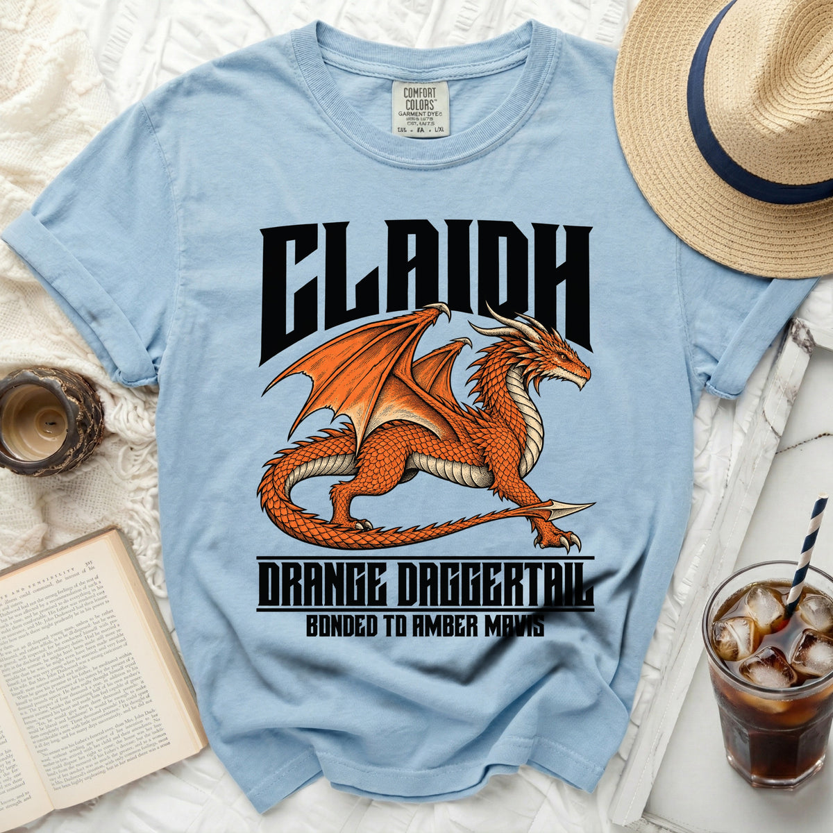 Light blue t-shirt with an orange dragon graphic and text "CLAIDH" and "ORANGE DAGGERTAIL BONDED TO AMBER MAVIS".