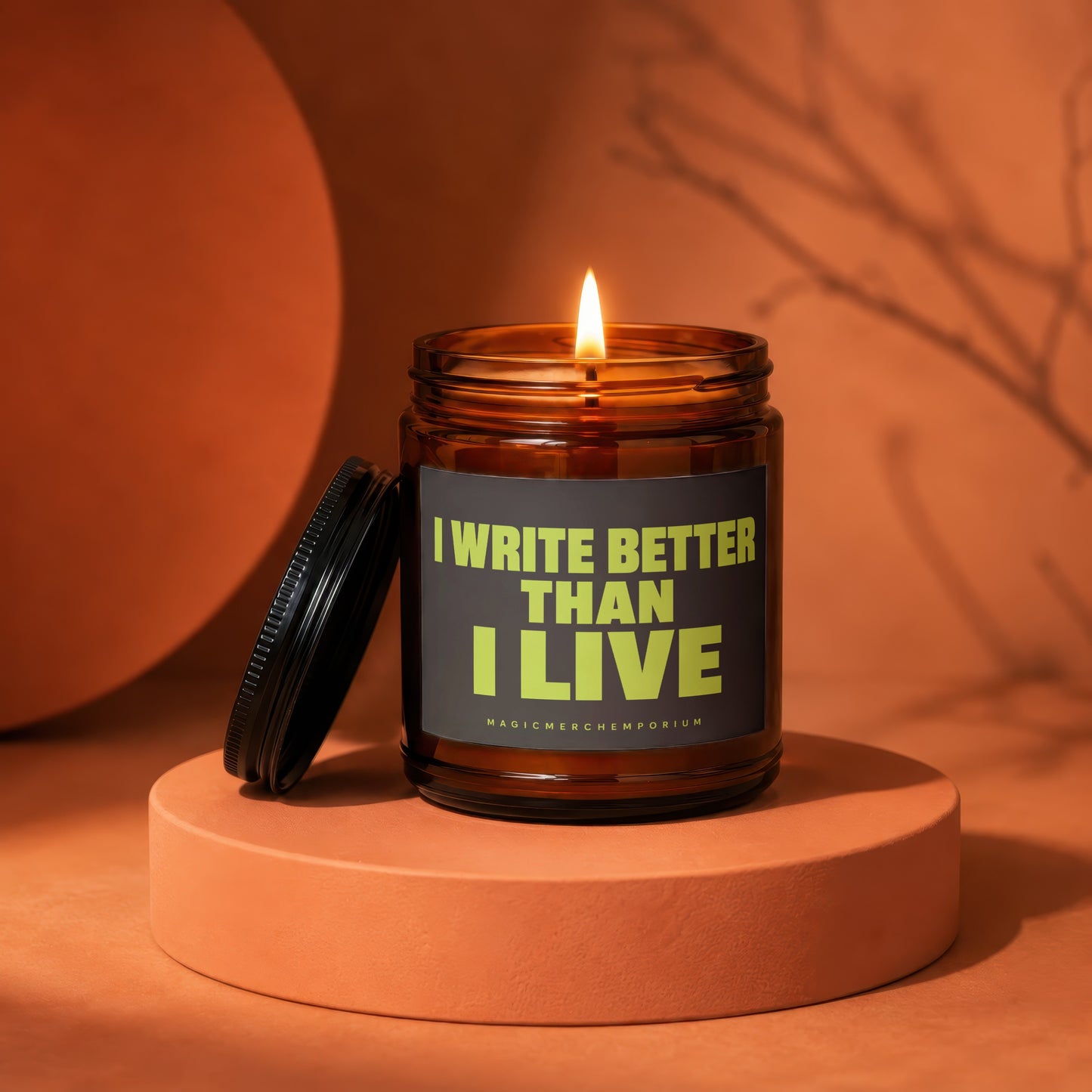 Amber jar candle with lit wick, dark label reads "I WRITE BETTER THAN I LIVE".
