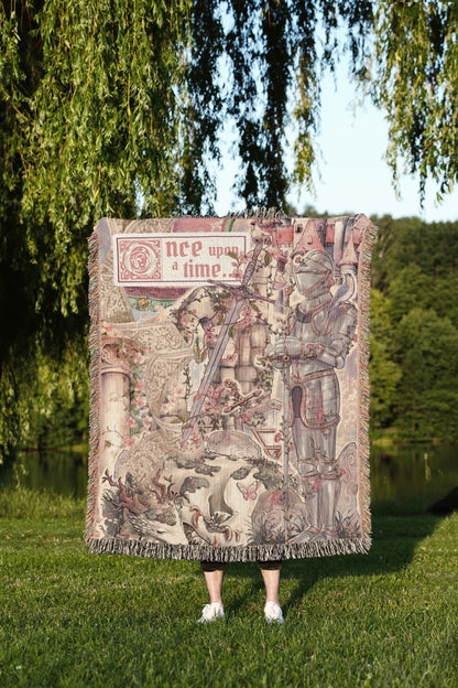 A person is standing in a grassy area, holding a large tapestry or blanket with a medieval-style illustration on it.
