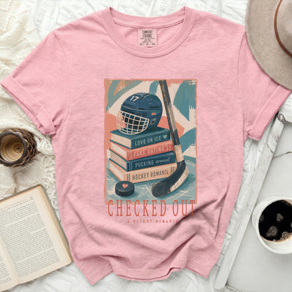 Pink t-shirt with "Checked Out A Hockey Romance" graphic of hockey gear and books.