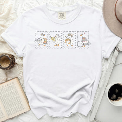 White t-shirt with four postage stamps featuring geese reading books.