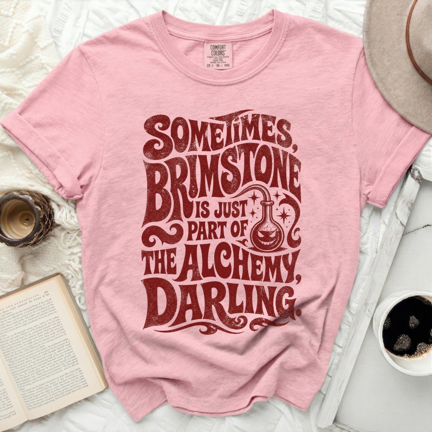 Pink t-shirt with "Sometimes Brimstone Is Part Of The Alchemy Darling" text.