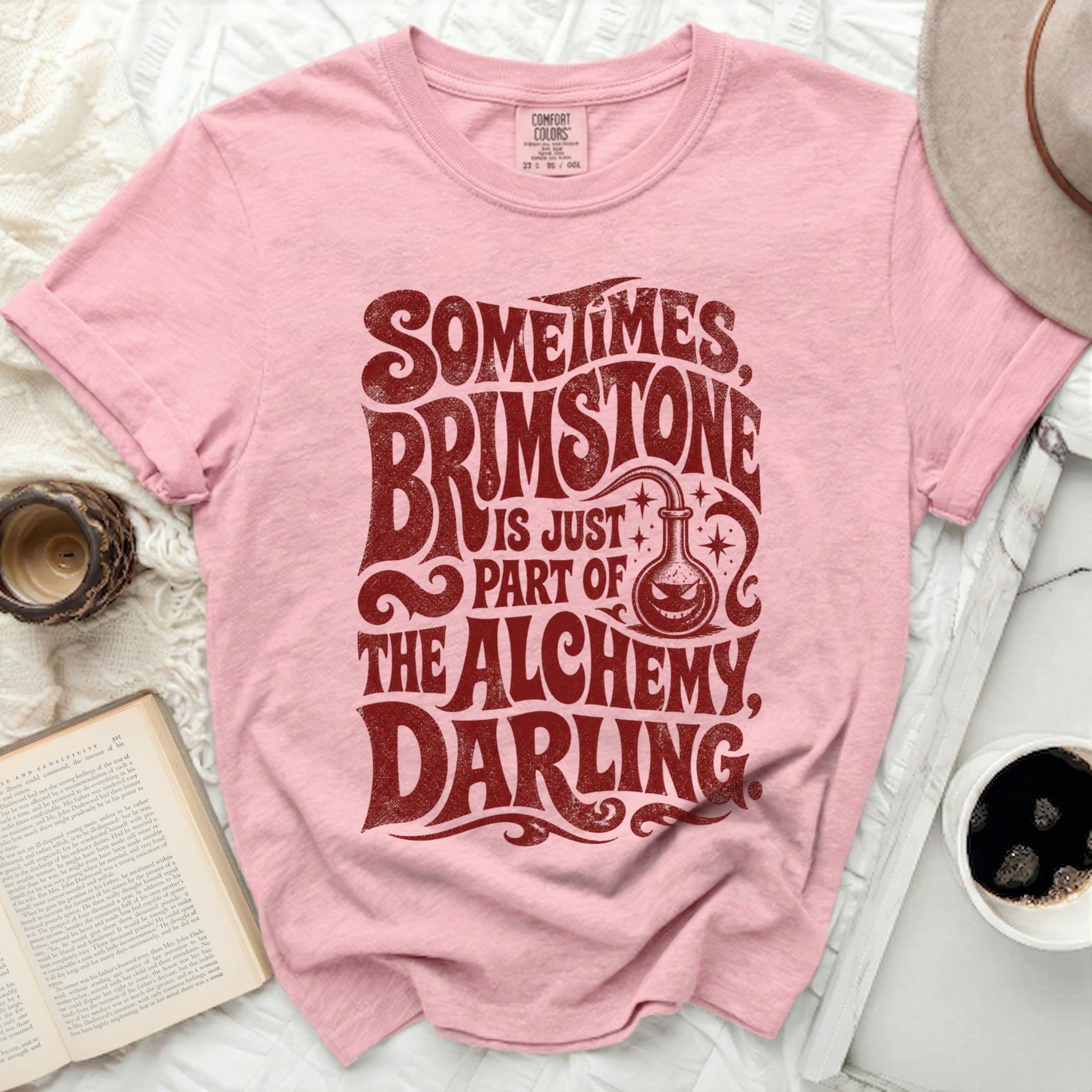 Pink t-shirt with "Sometimes Brimstone Is Part Of The Alchemy Darling" text.
