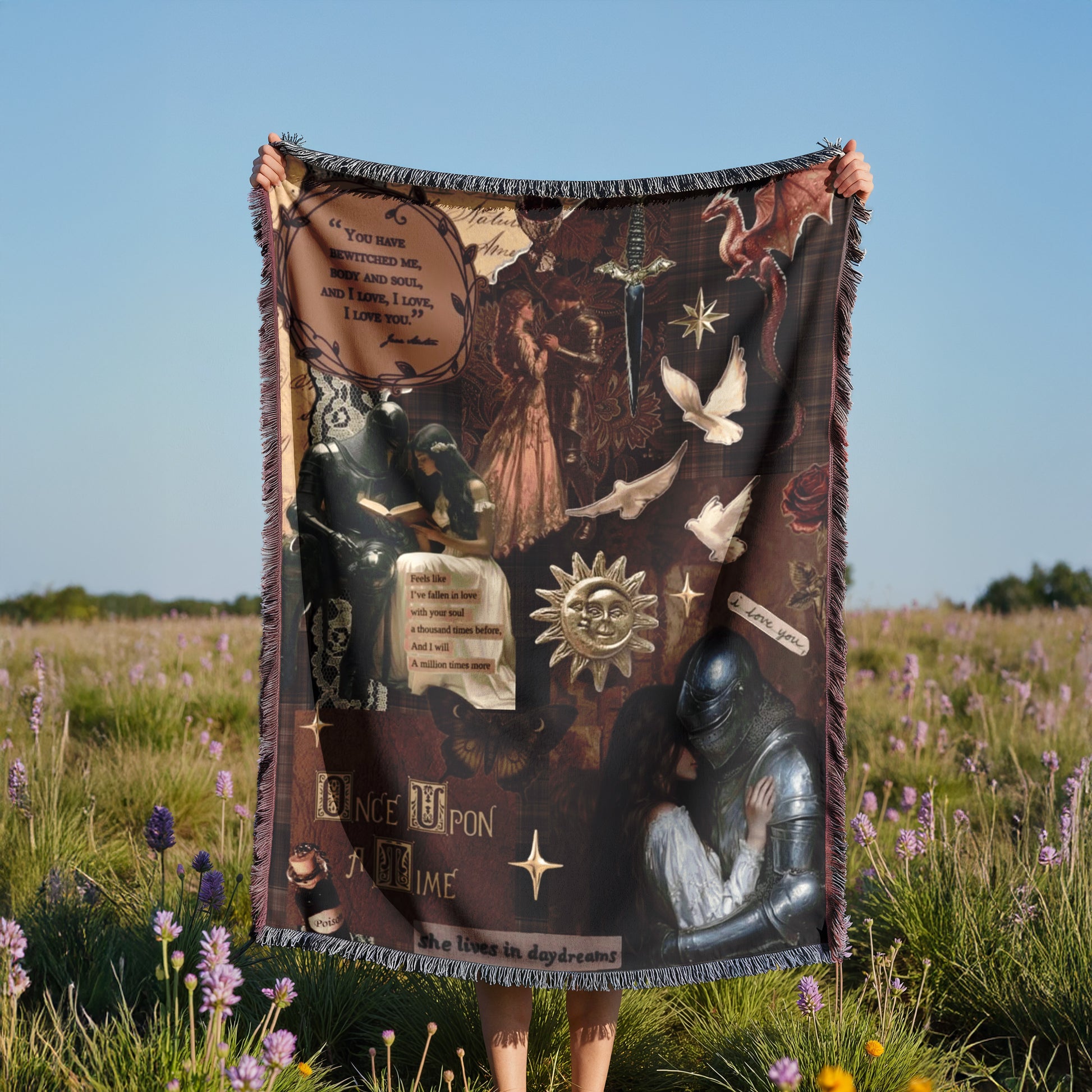 A person is holding up a large blanket with various images and text on it, standing in a field with purple flowers.