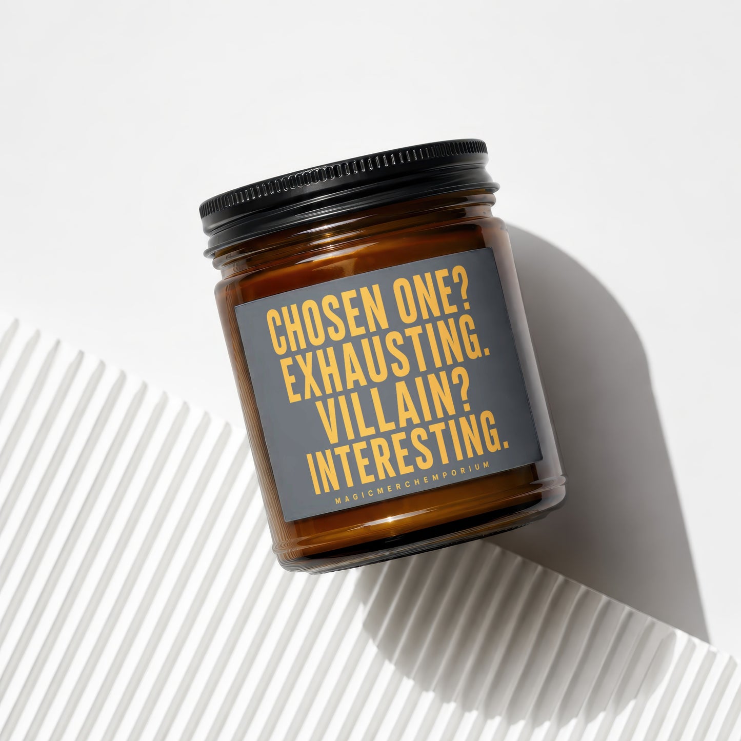 Amber jar candle with black lid and dark gray label saying "CHOSEN ONE? EXHAUSTING. VILLAIN? INTERESTING."
