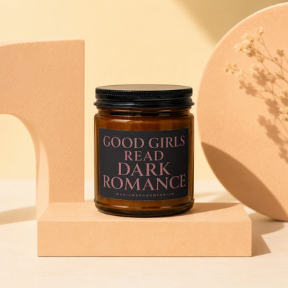 Amber glass candle with "GOOD GIRLS READ DARK ROMANCE" label on a pedestal.