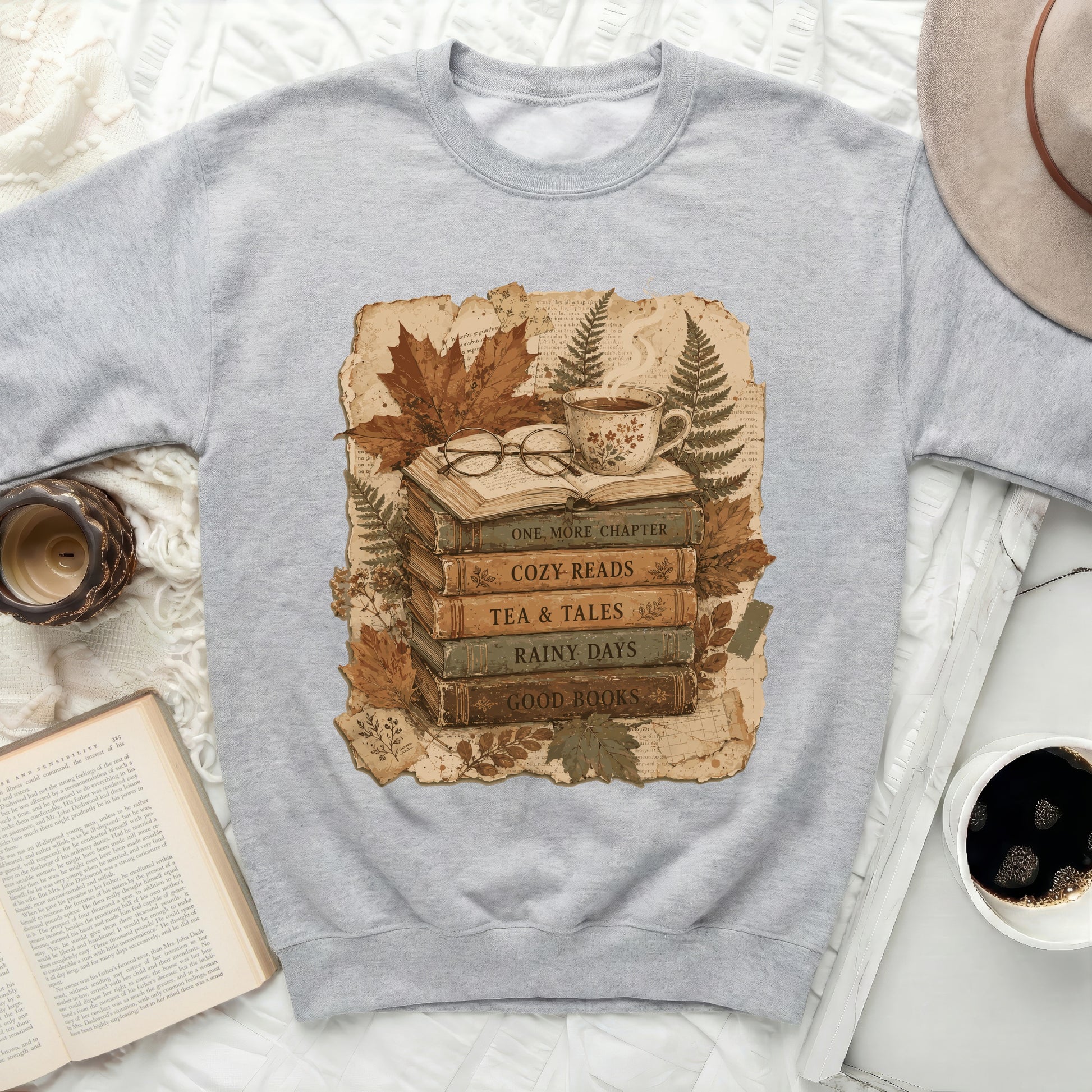 Gray sweatshirt with graphic of stacked books, cup of tea, glasses and autumn leaves.