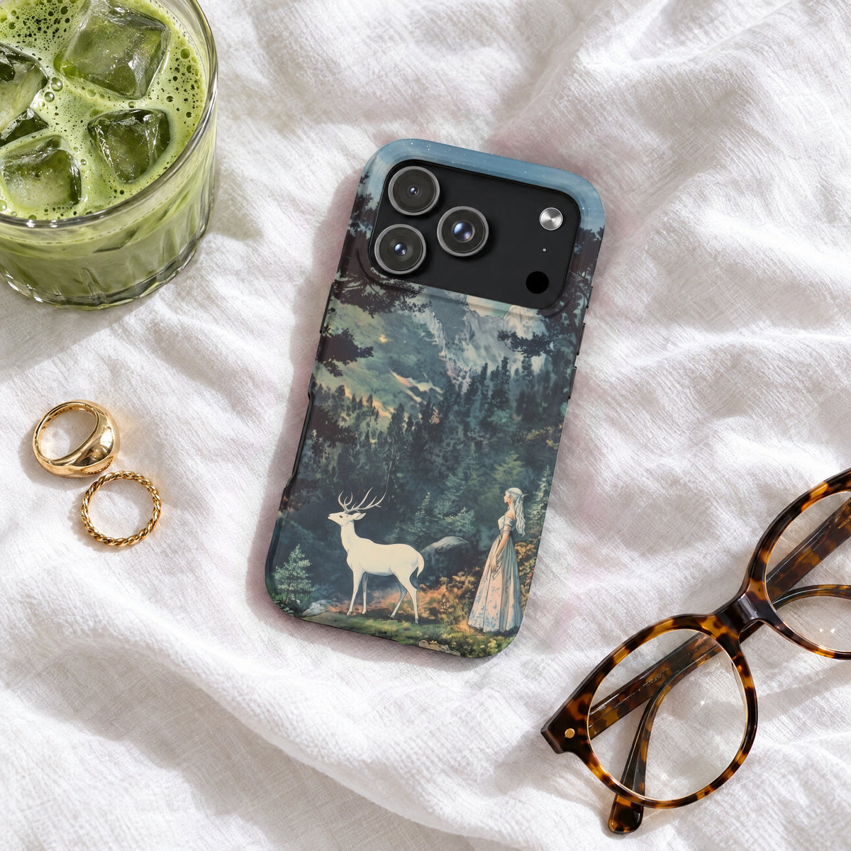 A smartphone case featuring a fantasy landscape with a white stag and woman, resting on white fabric.