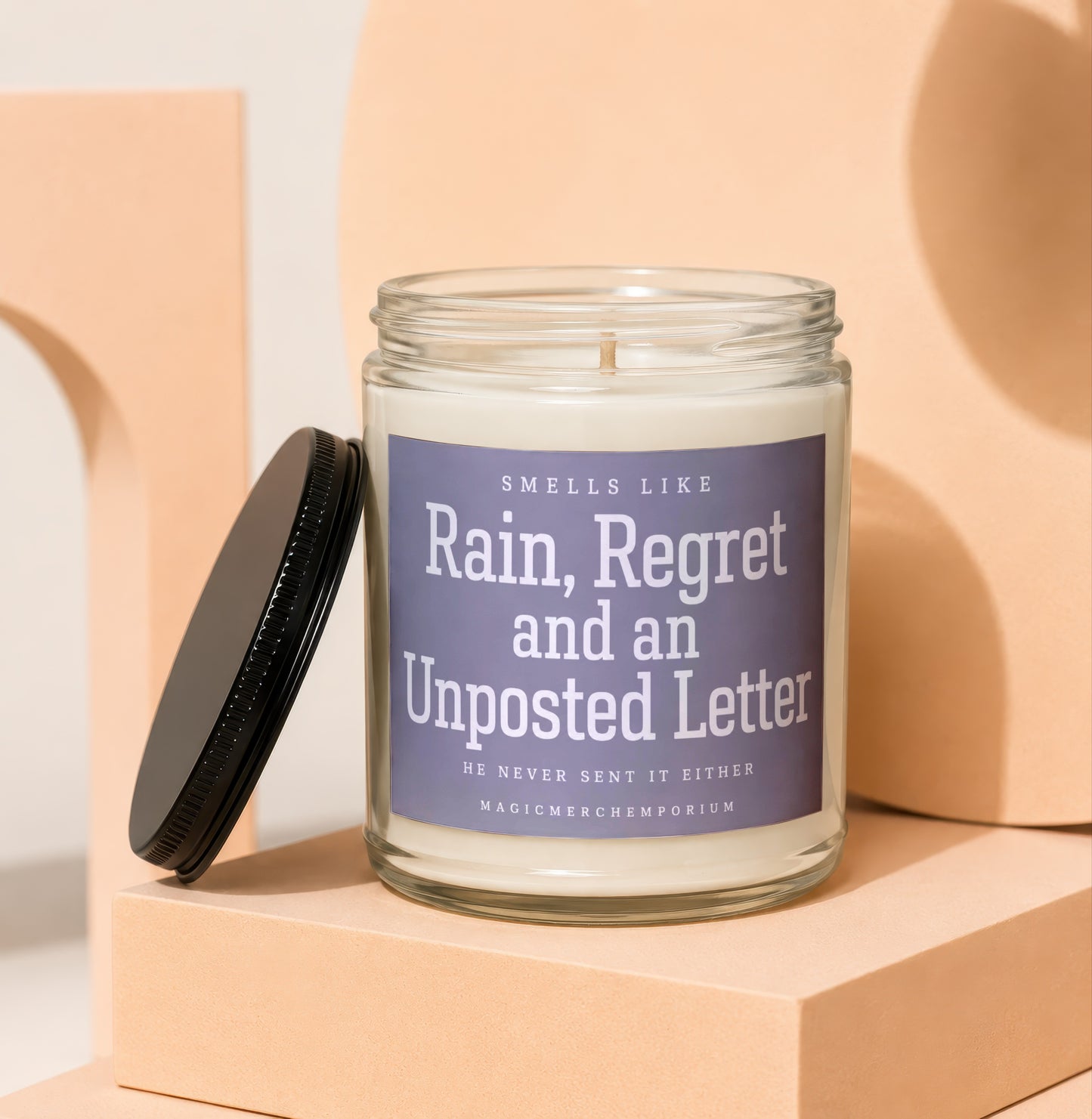 Glass jar candle with label reading "Smells Like Rain, Regret and an Unposted Letter".