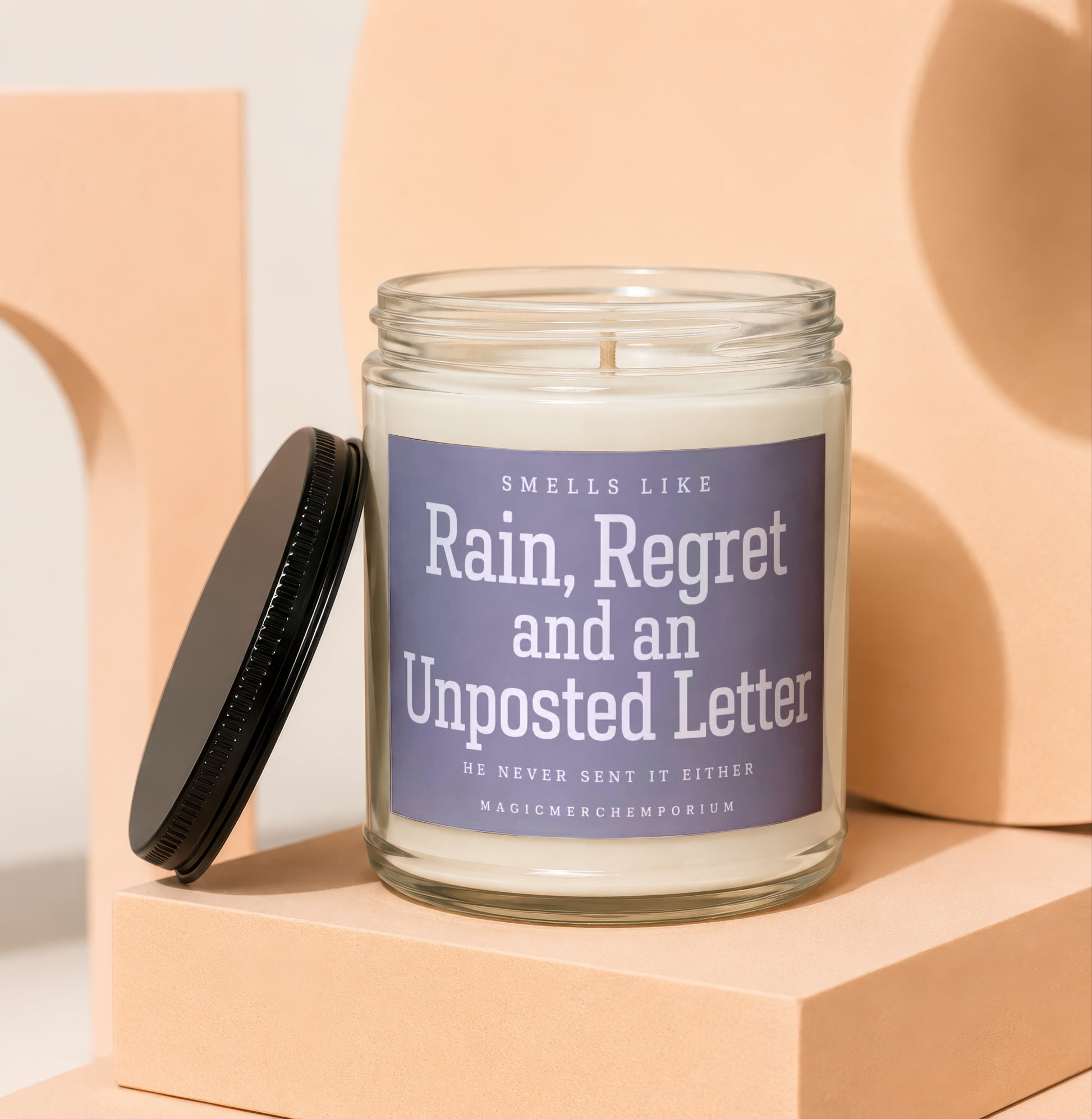 Glass jar candle with label reading "Smells Like Rain, Regret and an Unposted Letter".