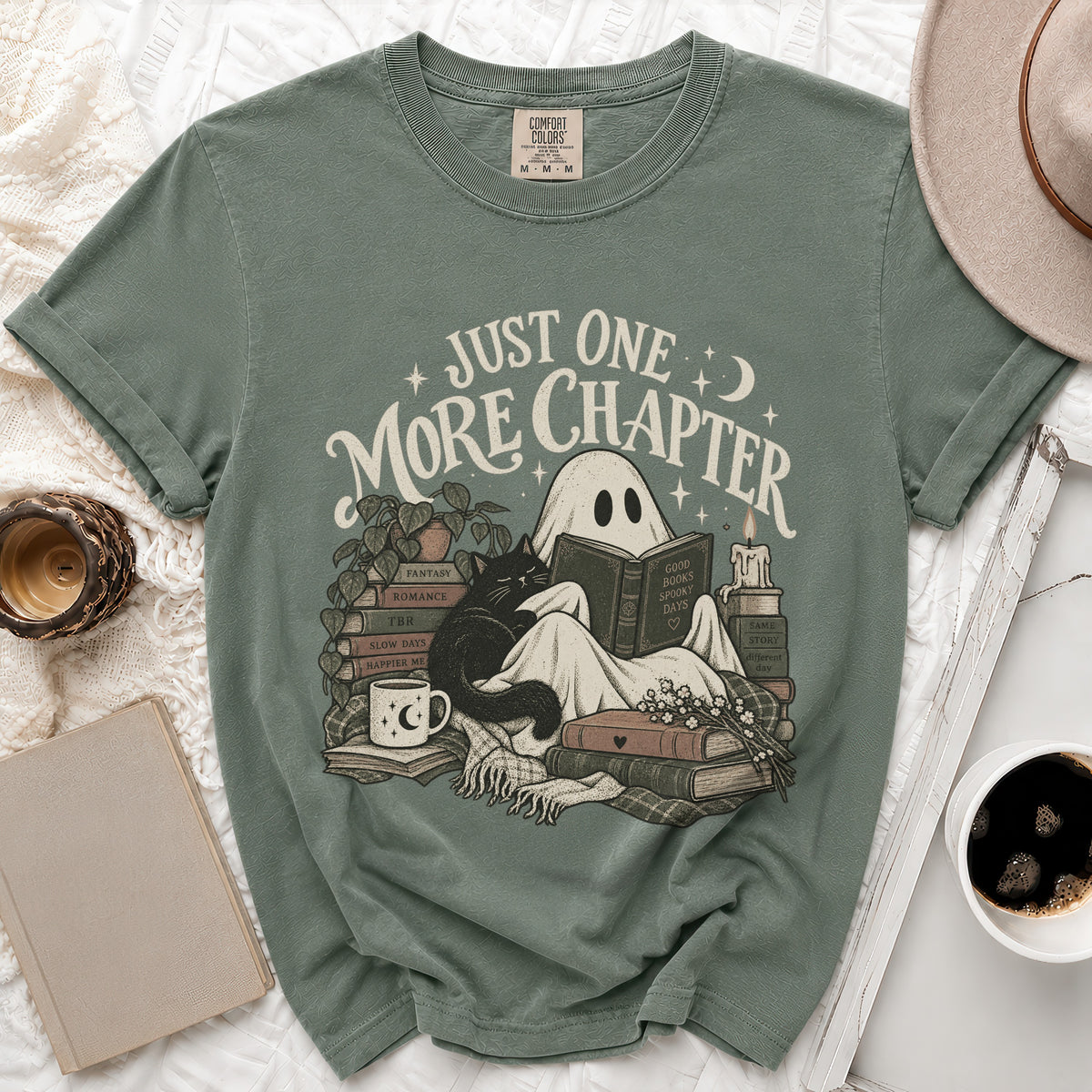Green t-shirt with ghost reading surrounded by books, cat, and mug. Text: "Just One More Chapter".