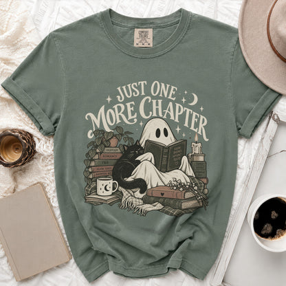 Green t-shirt with ghost reading surrounded by books, cat, and mug. Text: "Just One More Chapter".