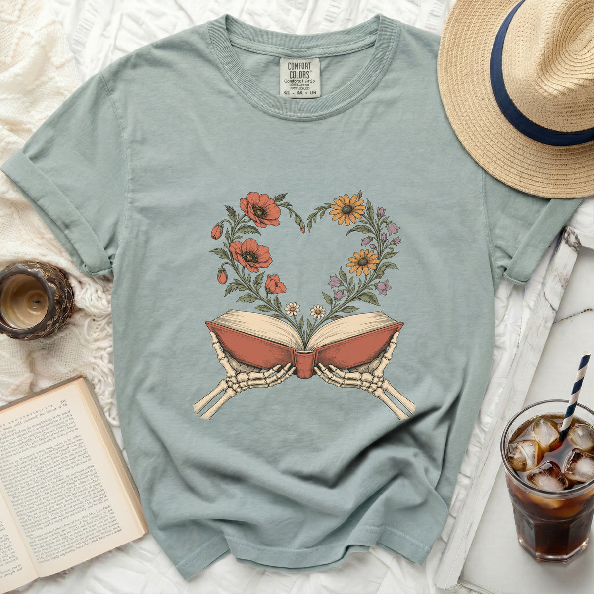 Skeleton hands hold open an antique book with flowers blooming in a heart shape.