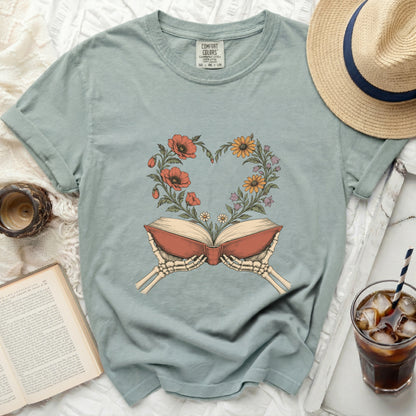 Skeleton hands hold open an antique book with flowers blooming in a heart shape.