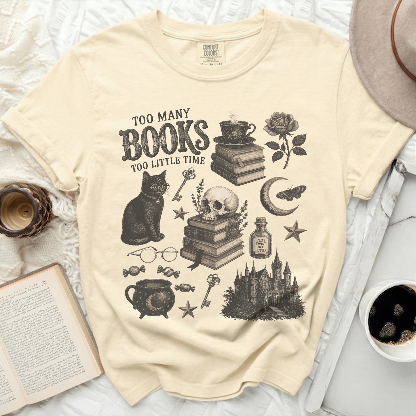 Cream t-shirt with graphic of cat, books, skull, cauldron, castle, and text "Too Many Books Too Little Time."
