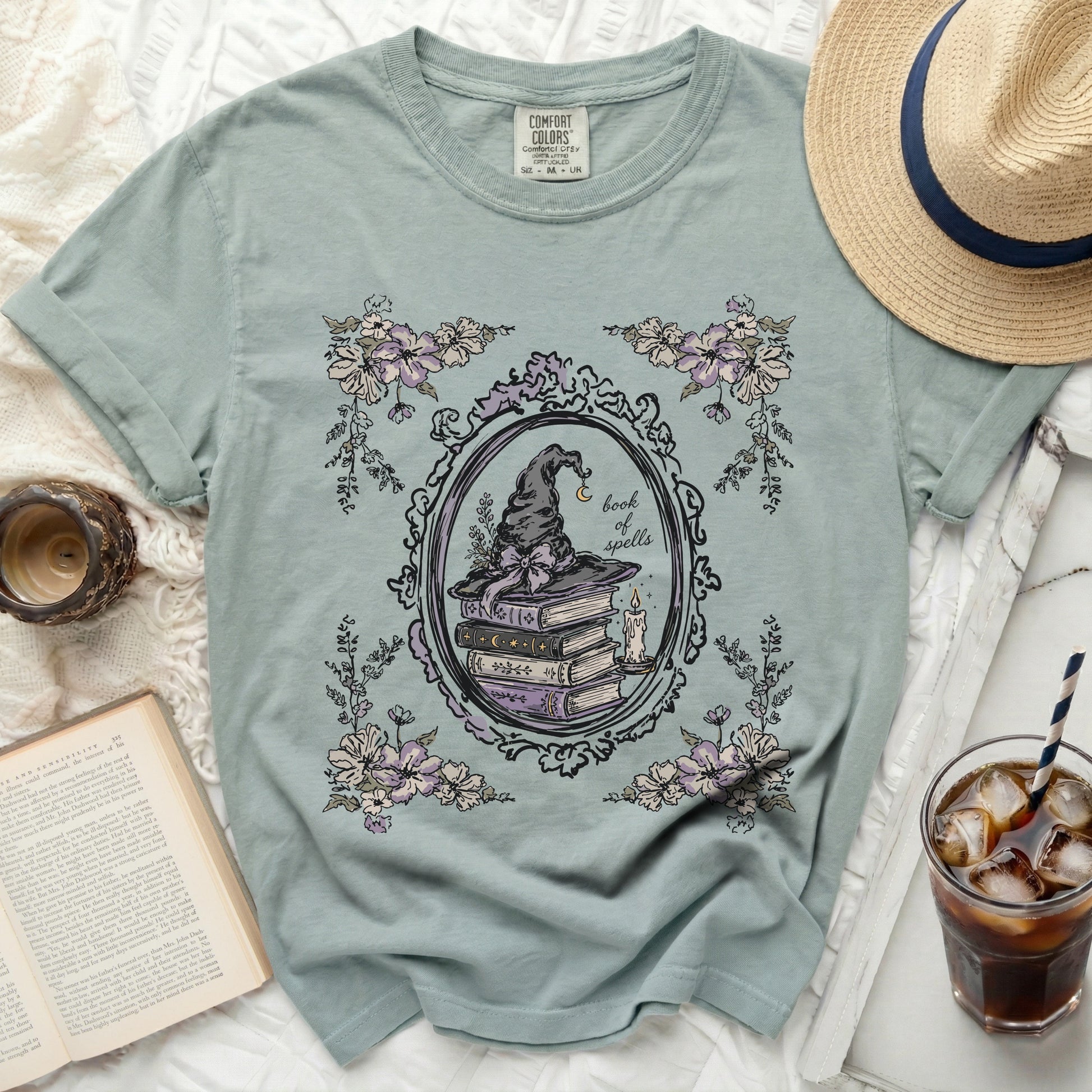 A blue t-shirt with a circular vintage frame graphic of a witch hat and books.