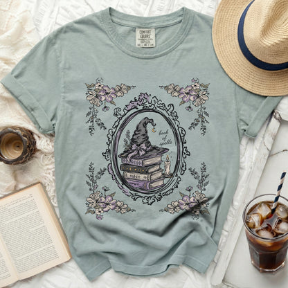 A blue t-shirt with a circular vintage frame graphic of a witch hat and books.