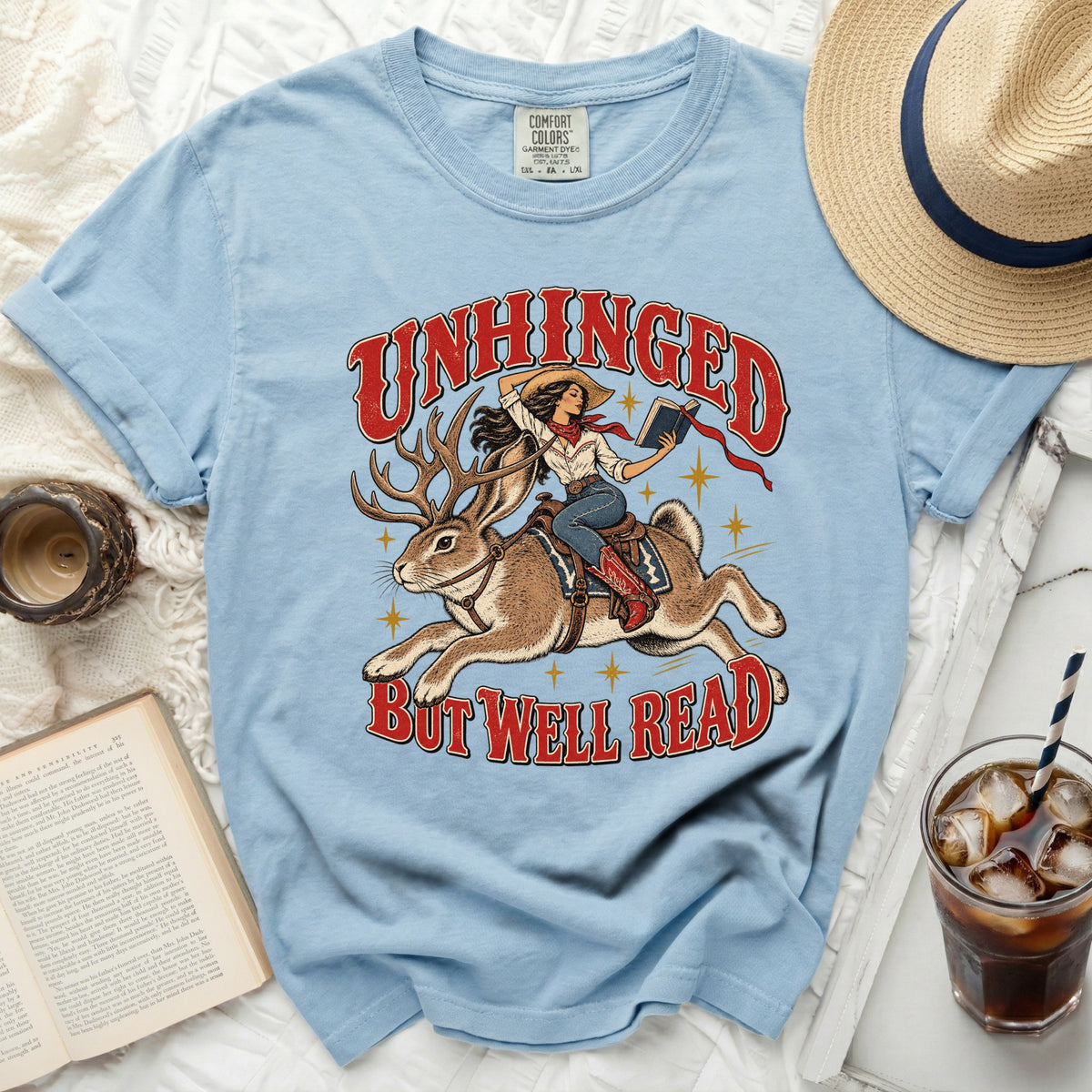 Light blue t-shirt with graphic of woman riding a jackalope, reading a book.