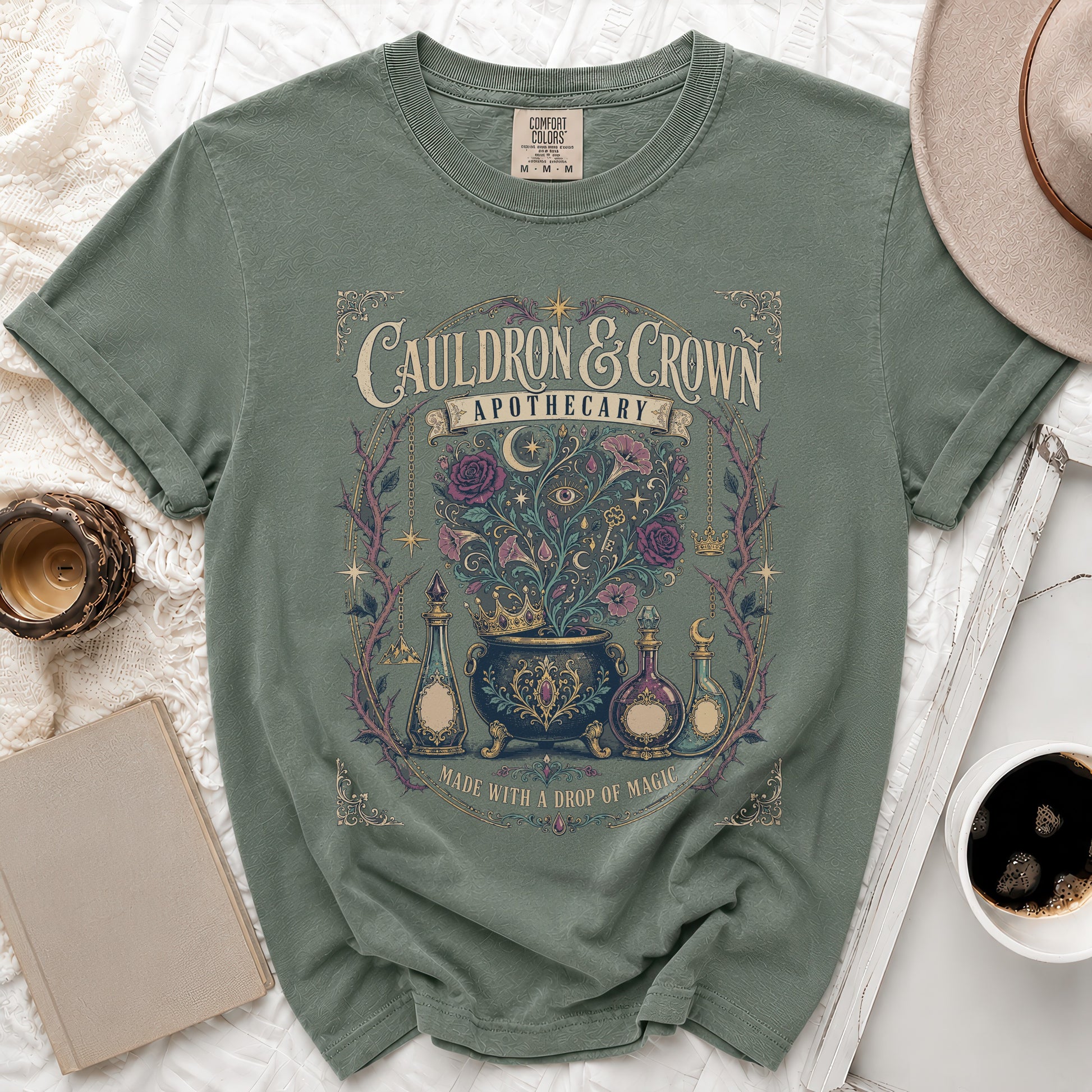 Green t-shirt with "Cauldron & Crown Apothecary" and mystical artwork.