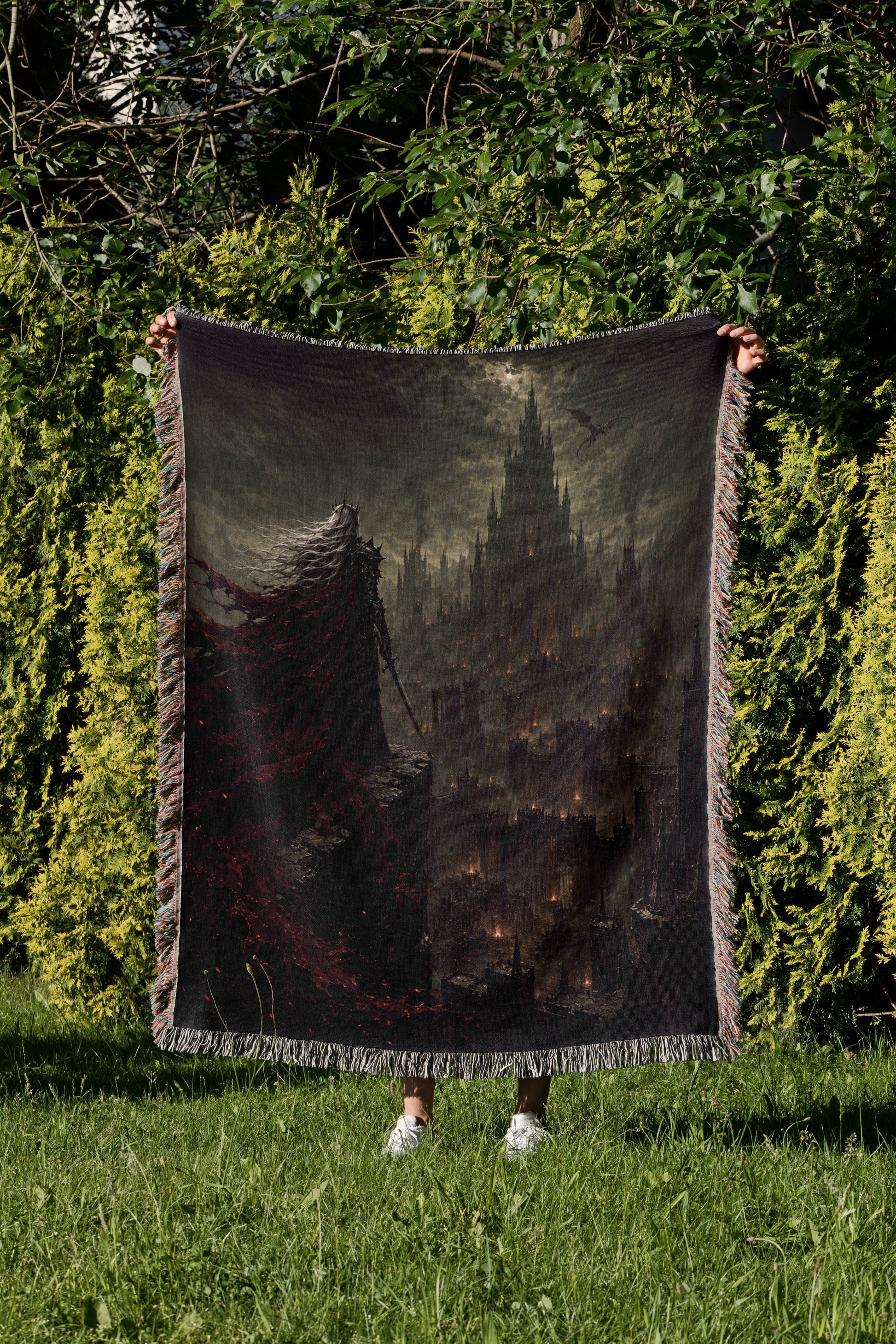 A person is standing in a grassy area, holding up a large blanket that features a dark, ominous castle-like scene.