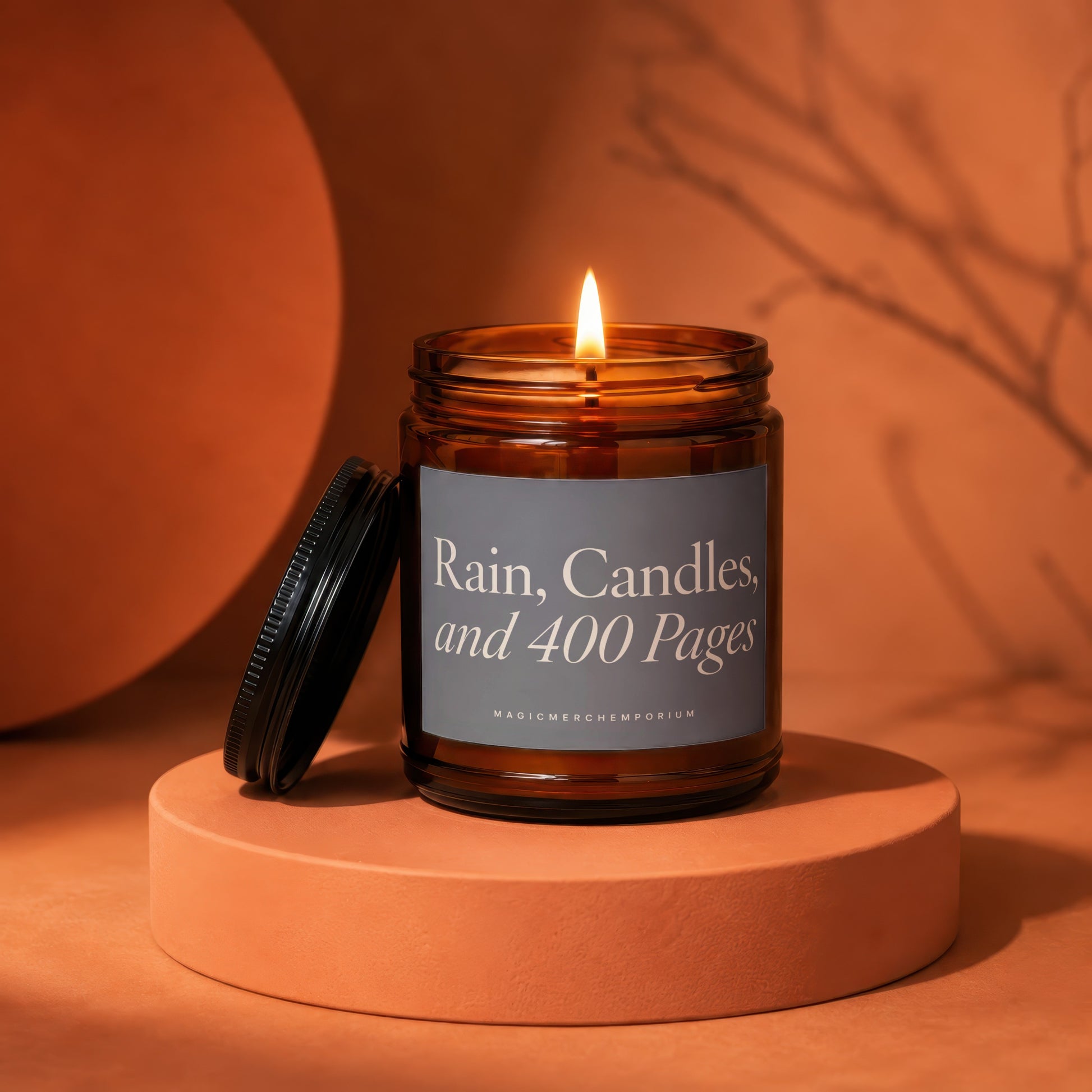 Amber glass candle with lit wick and label "Rain, Candles, and 400 Pages".