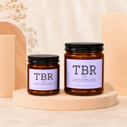 Two amber glass candles labeled "TBR" sit on a display with text about books.