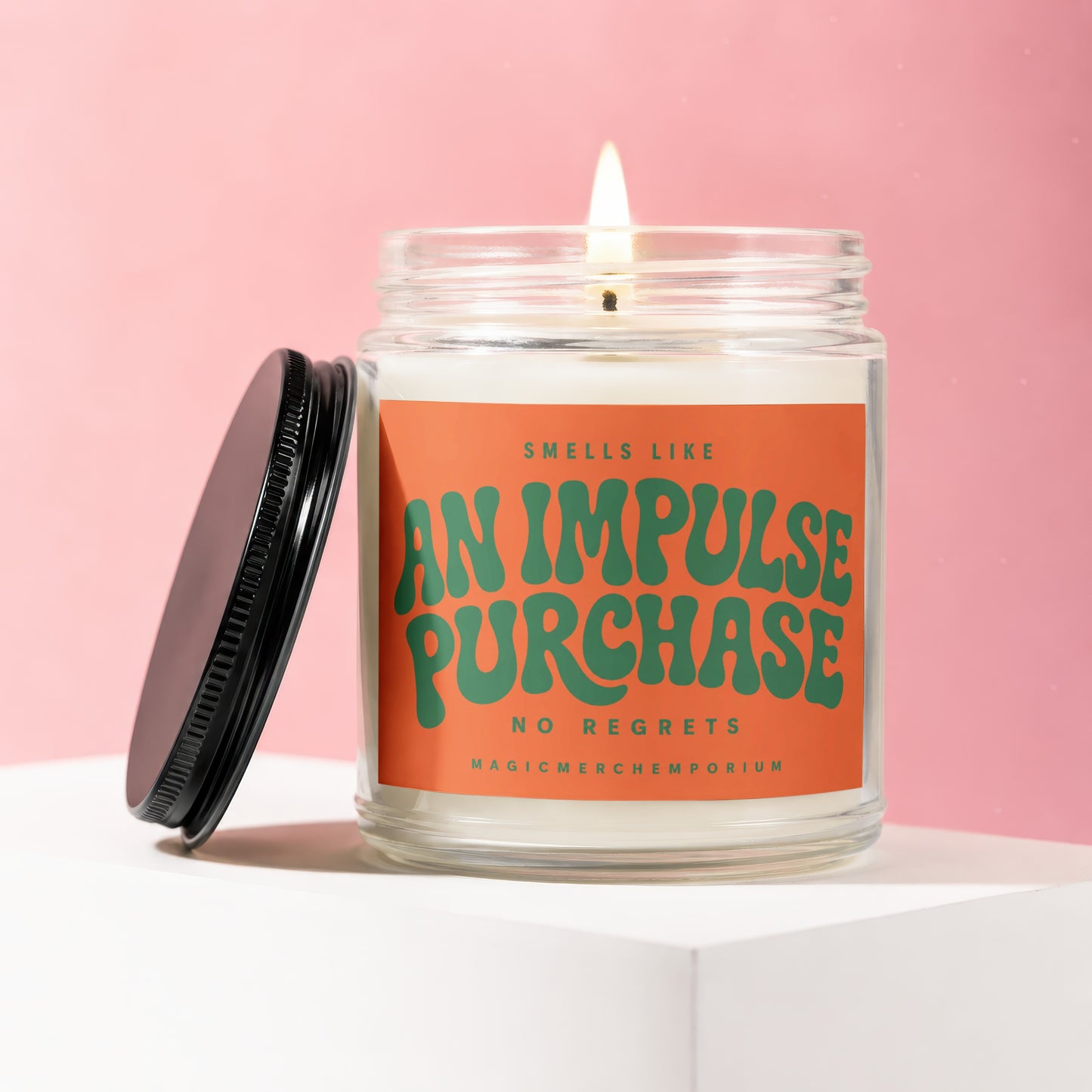 Lit candle in a glass jar with an orange label reading "Smells Like An Impulse Purchase No Regrets".