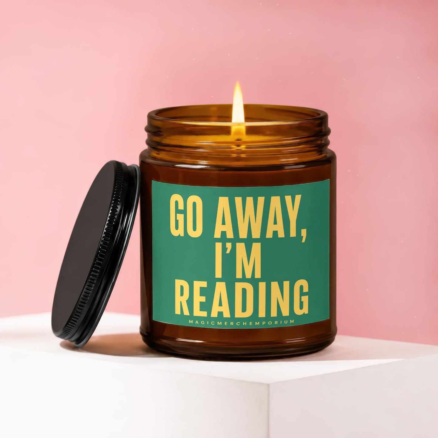 Amber glass candle with lit flame and black lid, reads "GO AWAY, I'M READING".
