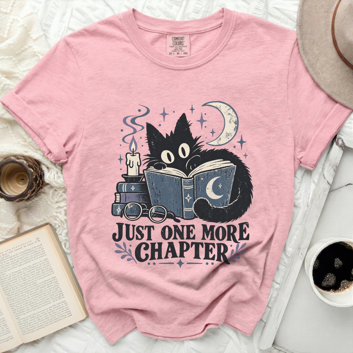Pink t-shirt with graphic of black cat reading book, moon, candle, and text "Just One More Chapter".