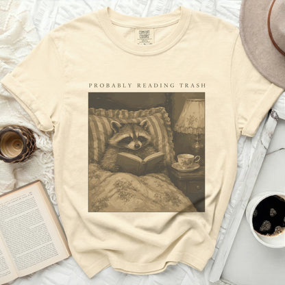 T-shirt with raccoon reading a book next to a lamp and tea cup.