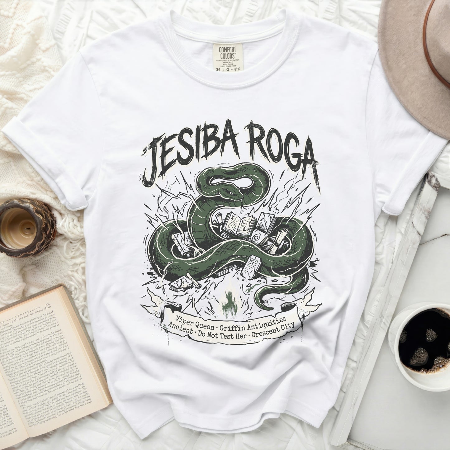 White t-shirt with green snake, books, and text "JESIBA ROGA".
