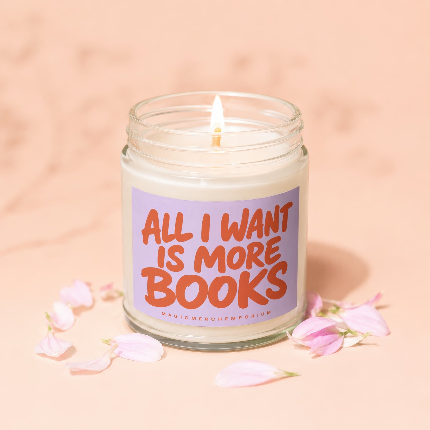 Jar candle with lit wick and label reading "ALL I WANT IS MORE BOOKS MAGICMERCH".