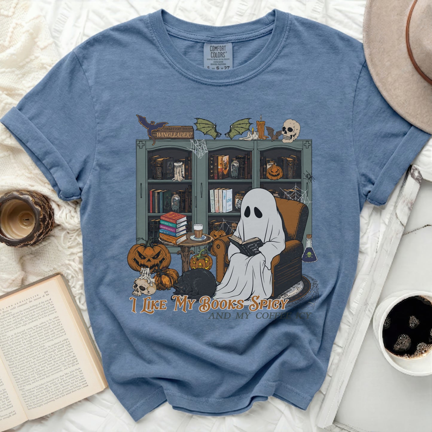 Ghost reading by bookshelf with pumpkins, text says "I like my books spicy and my coffee icy."