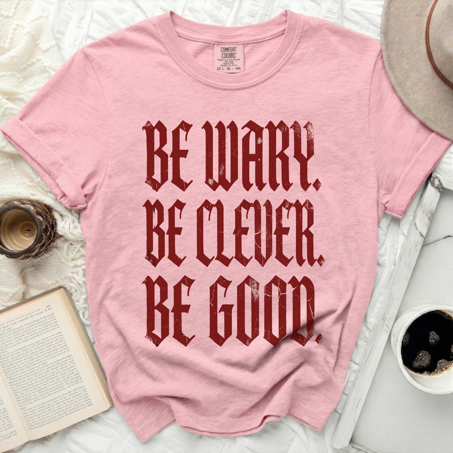 Pink t-shirt with burgundy text "BE WARY. BE CLEVER. BE GOOD."