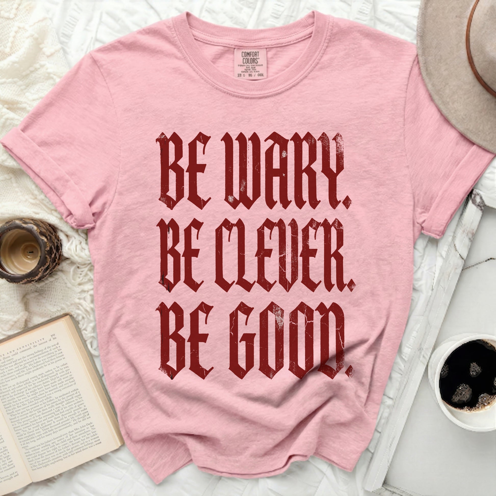 Pink t-shirt with burgundy text "BE WARY. BE CLEVER. BE GOOD."