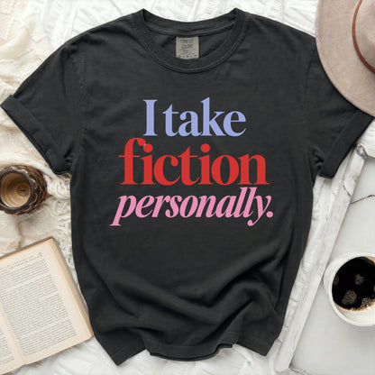 A black crewneck t-shirt with the text "I take fiction personally." printed in multi-colored serif letters.