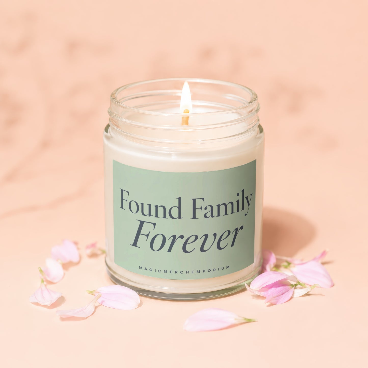 Lit candle in glass jar with "Found Family Forever" label and pink petals around base.