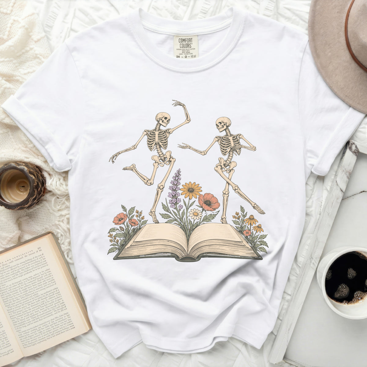 White t-shirt with dancing skeletons and flowers on an open book graphic.