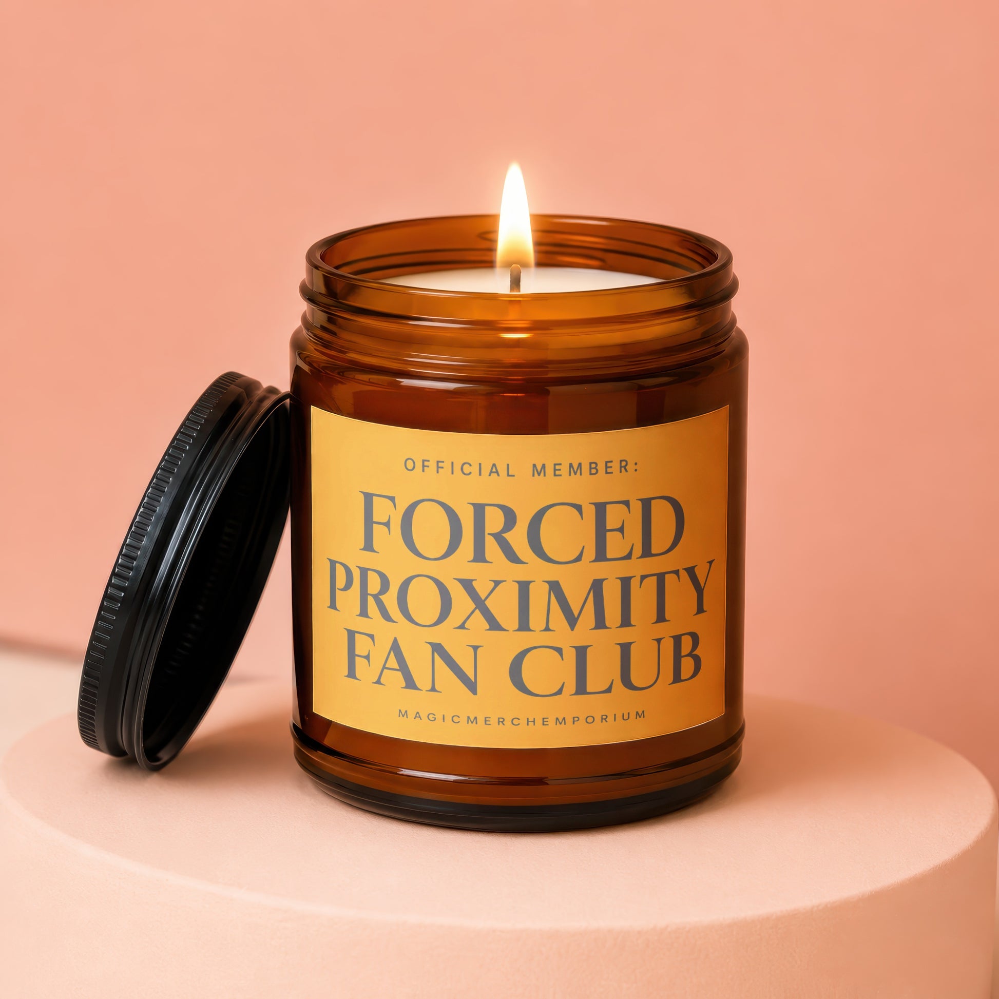 Amber glass candle with lit flame and black lid, labeled Forced Proximity Fan Club.