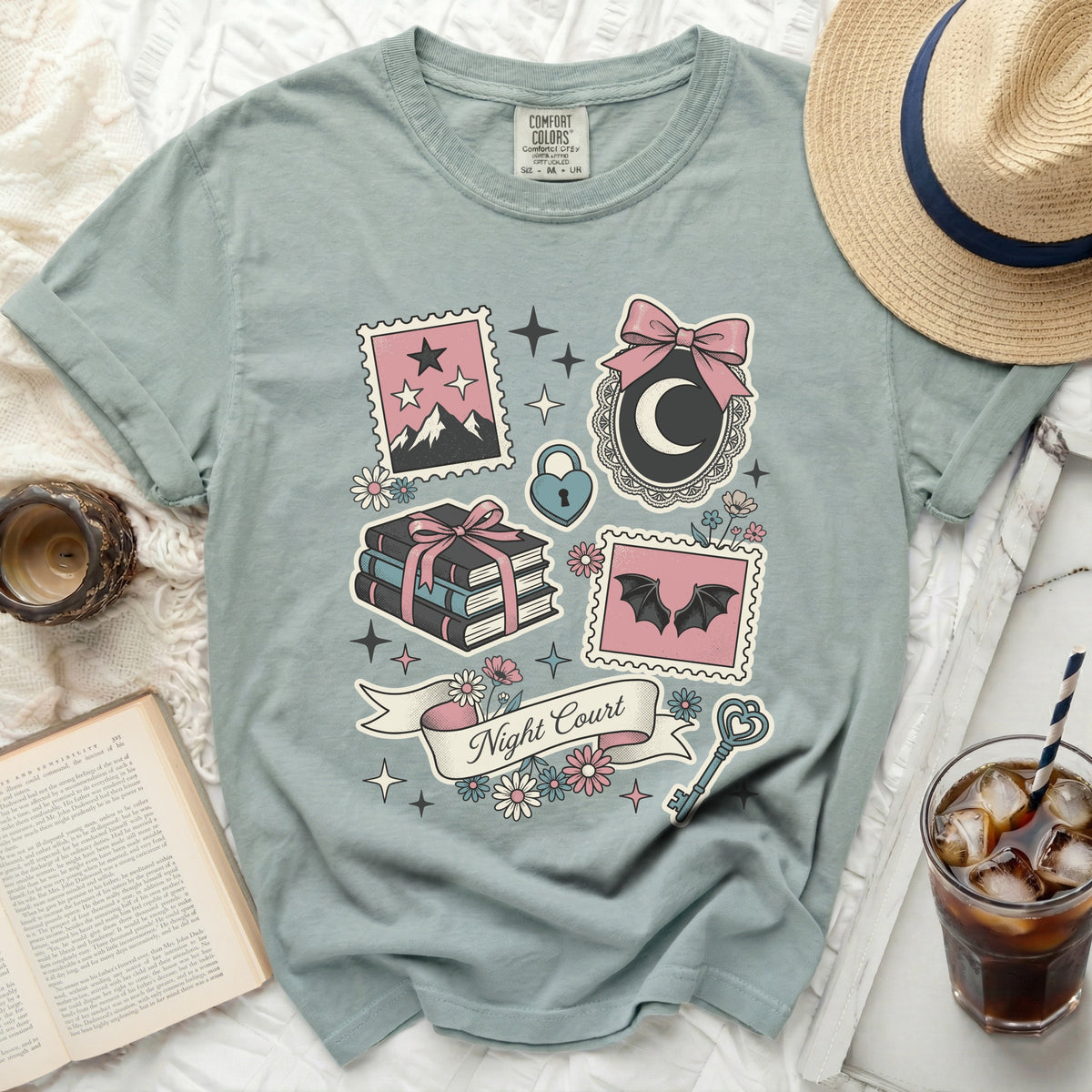 Light blue t-shirt with "Night Court" and graphic designs of stamps, books, moon, bats, and flowers.