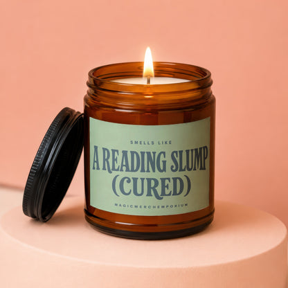 Amber jar candle with lit wick, labeled "Smells Like A Reading Slump (Cured)".